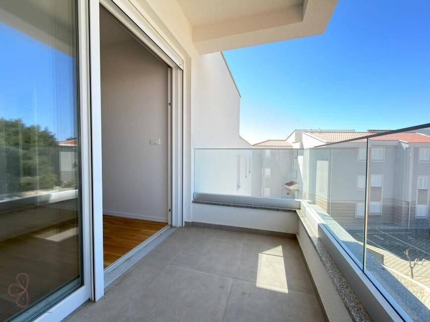 Heller Balkon mit Glasgeländer und Blick auf die umliegenden Gebäude und den Himmel.