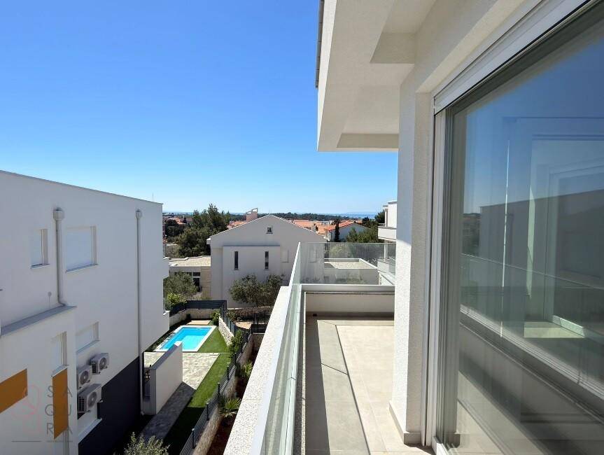 Balkon mit Glasgeländer und Blick auf einen kleinen Pool und die umliegende Landschaft.