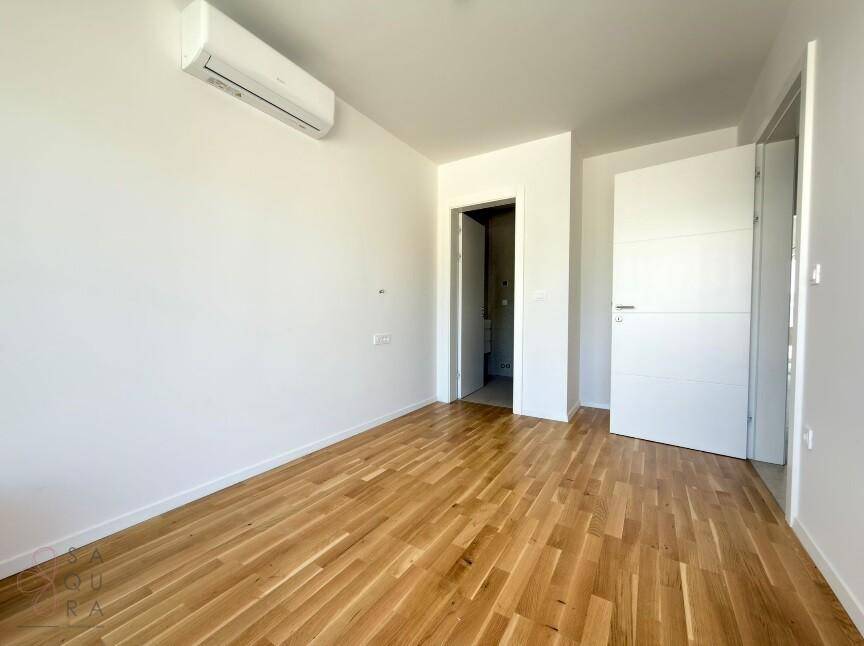 Heller Raum mit Holzboden, Klimaanlage und Zugang zu einem Badezimmer.