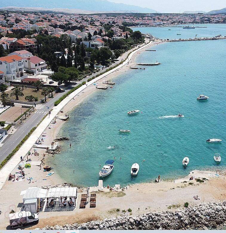 Panoramablick auf die belebte Küste mit Sandstrand, türkisblauem Meer und Booten.