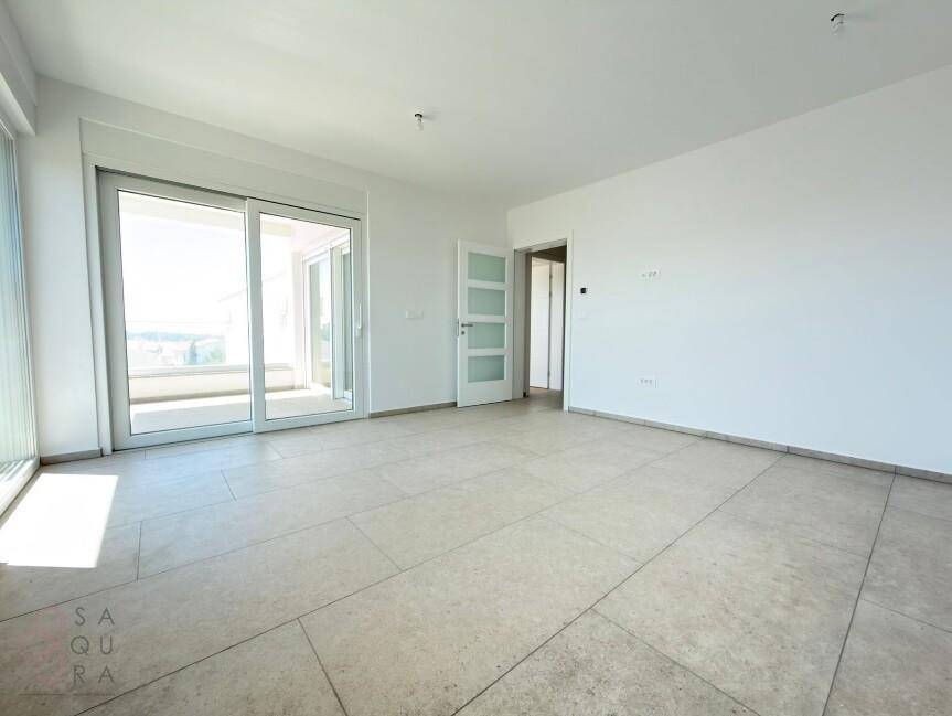 Heller Raum mit Fliesenboden und Schiebetüren, die zu einem sonnigen Balkon führen.