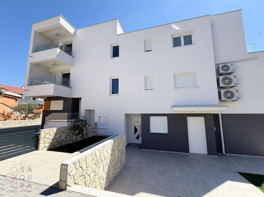 Außenansicht eines modernen Gebäudes mit Klimaanlagen an der Fassade und gepflastertem Zugang.
