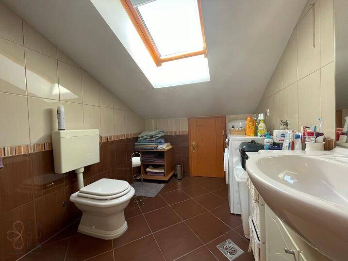 Badezimmer mit Fliesen, Toilette, Waschbecken und einem Dachfenster für Tageslicht.