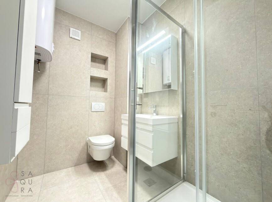 Modernes Badezimmer mit WC, Duschkabine, Waschtisch und Spiegelschrank in hellen Fliesen.