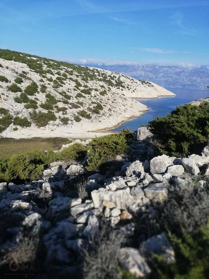 Felsige Küstenlandschaft mit Blick auf eine ruhige Bucht und das offene Meer unter klarem Himmel.