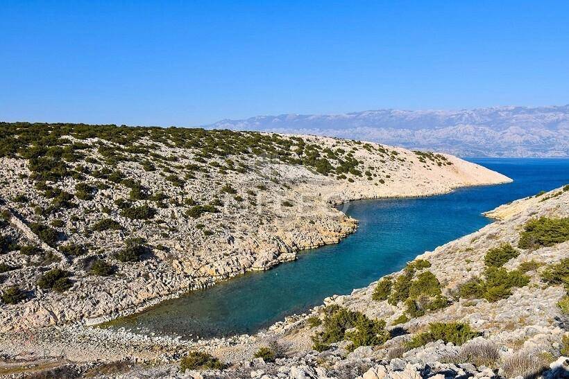 Malerische Küstenlandschaft mit klarem blauen Wasser und karger Felsformation unter einem weiten Himmel.