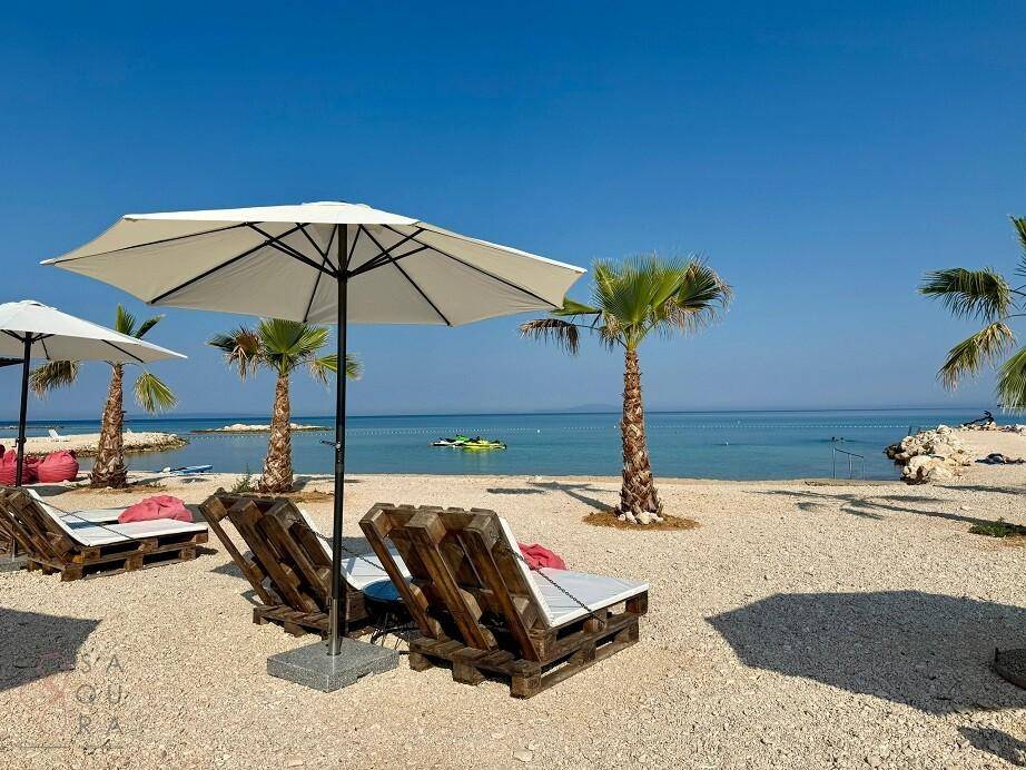 Entspannter Strandbereich mit Liegestühlen, Sonnenschirmen und Palmen am klaren Meer.
