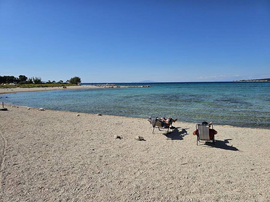Ruhiger Strandabschnitt mit zwei Liegestühlen und klarem, flachem Meerwasser.