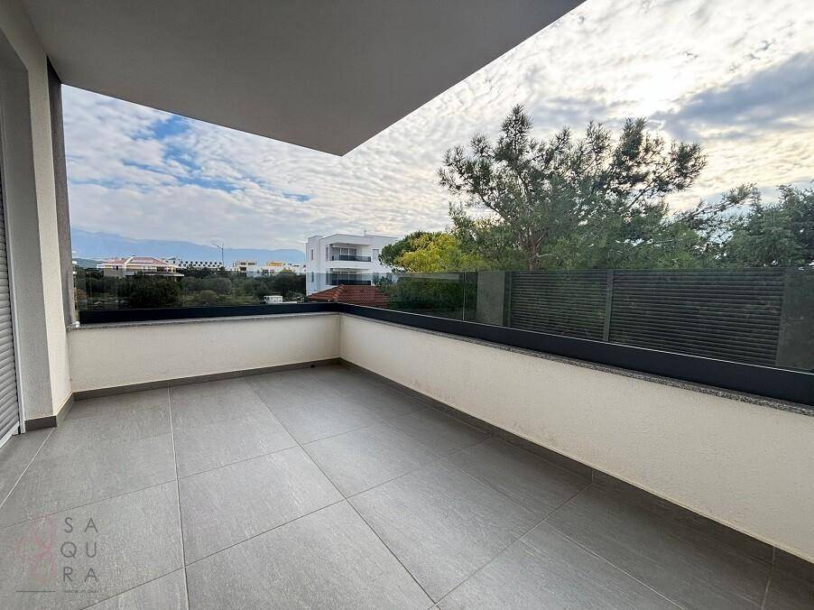 Geräumiger Balkon mit modernen grauen Fliesen, Glasgeländer und Blick ins Grüne.