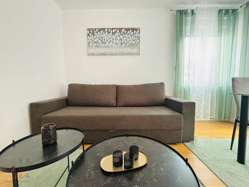 Gemütliches Wohnzimmer mit braunem Sofa, modernen Couchtischen und hellgrünen Vorhängen.