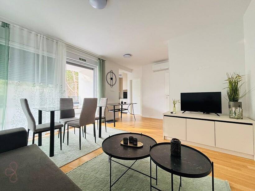 Offener Wohn-Essbereich mit hellem Parkettboden, modernen Möbeln und Zugang zum Balkon.