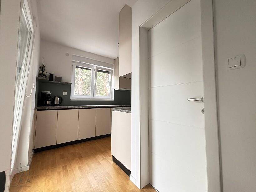 Küchenecke mit Fenster, modernen Schränken und einer weißen Tür.