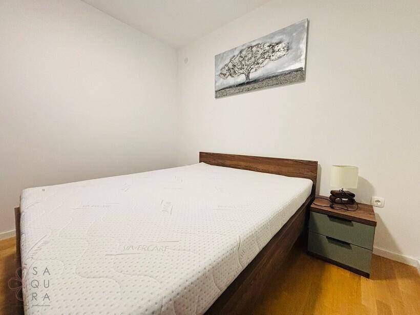 Helles Schlafzimmer mit Holzbett, weißer Matratze und modernem Nachttisch.