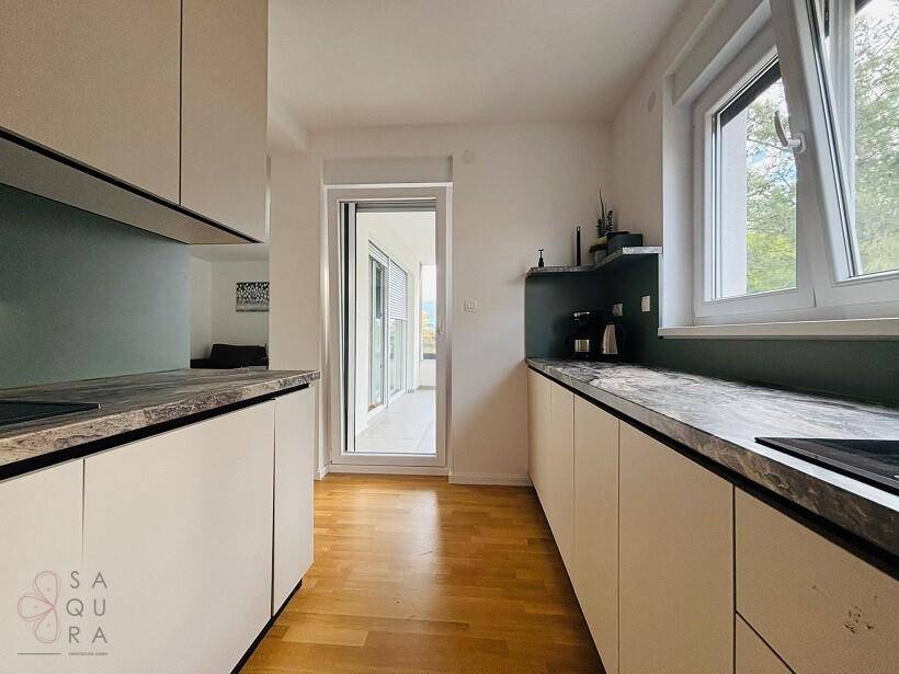 Helle Küche mit Fenster, modernen Einbauschränken und Zugang zu einem Außenbereich.