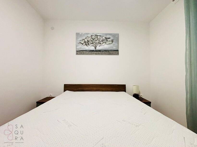 Schlafzimmer mit Holzbettrahmen, weißer Matratze und einem dekorativen Wandbild.