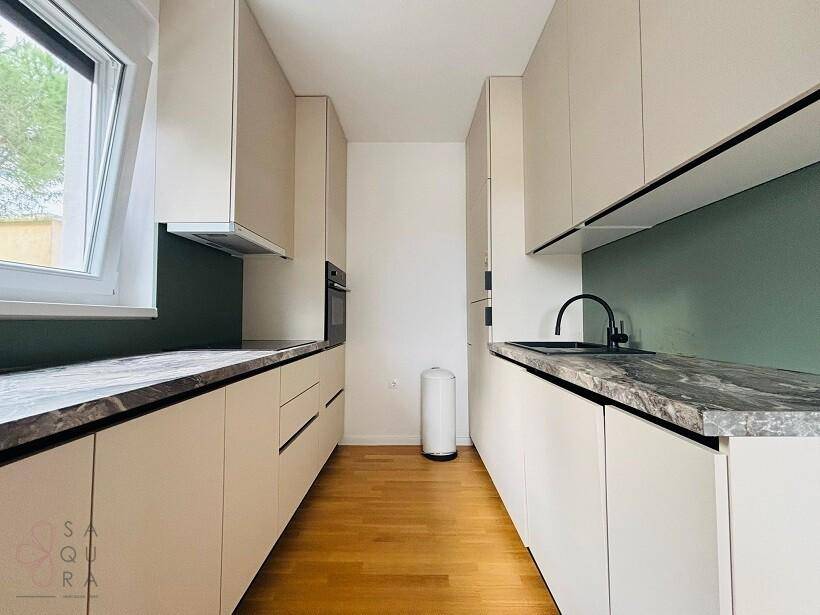 Moderne Küche mit beigen Schränken, dunklen Arbeitsplatten und Fenster für Tageslicht.
