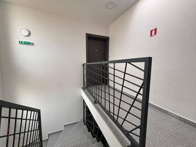 Modernes Treppenhaus mit grauem Boden, weißen Wänden und schwarzem Metallgeländer.