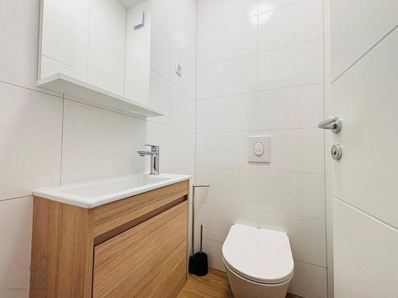 Modernes Gäste-WC mit weißen Fliesen, Holzwaschtisch und integriertem Spiegel.