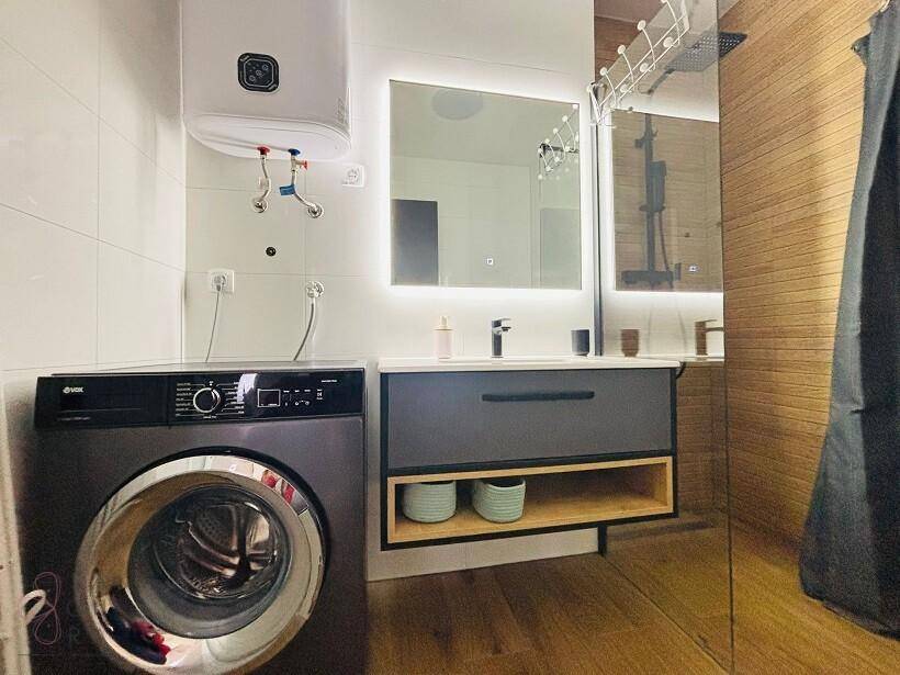 Modernes Badezimmer mit Waschmaschine, beleuchtetem Spiegel und dunklem Waschtischunterschrank.