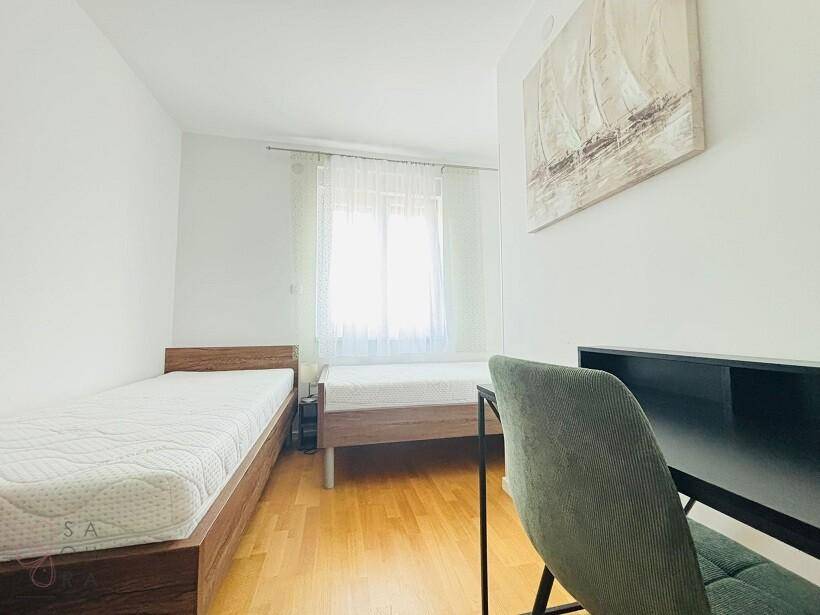 Helles Schlafzimmer mit zwei Einzelbetten, Schreibtisch und Fenster mit Vorhängen.