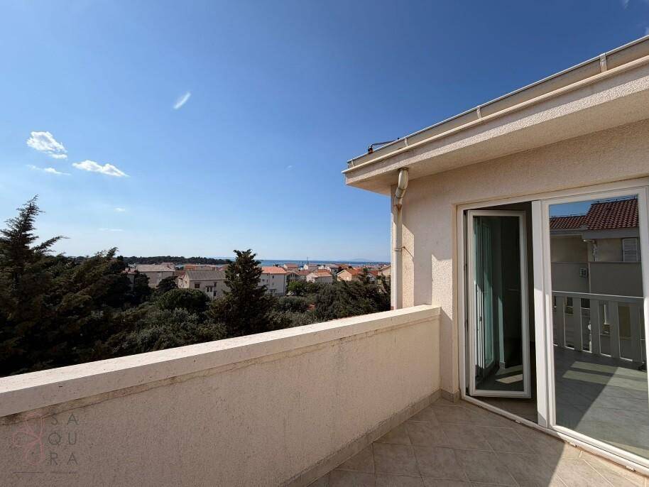 Heller Balkon mit Fliesenboden und weitem Blick über Dächer und Bäume bis zum Meer.
