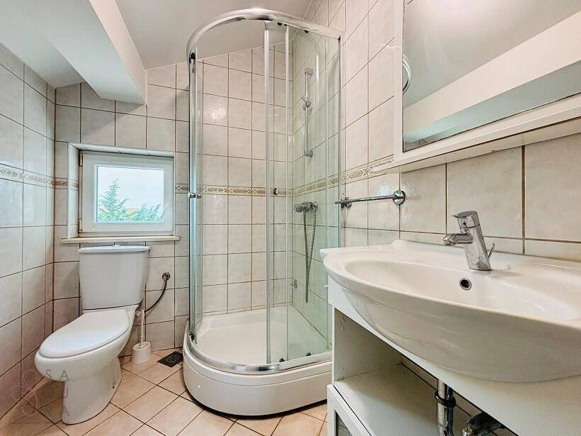 Badezimmer mit Eckdusche, Toilette, Waschbecken und gefliesten Wänden und Boden.
