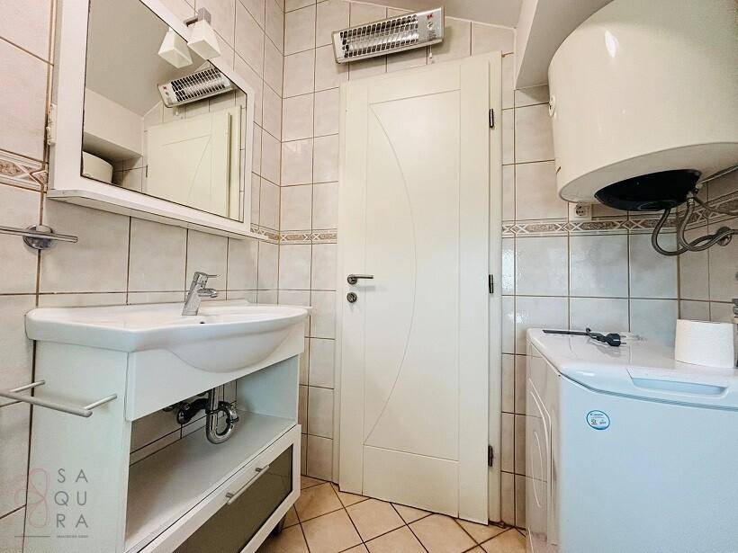 Badezimmer mit Waschbecken, Spiegel, Waschmaschine und Warmwasserboiler.
