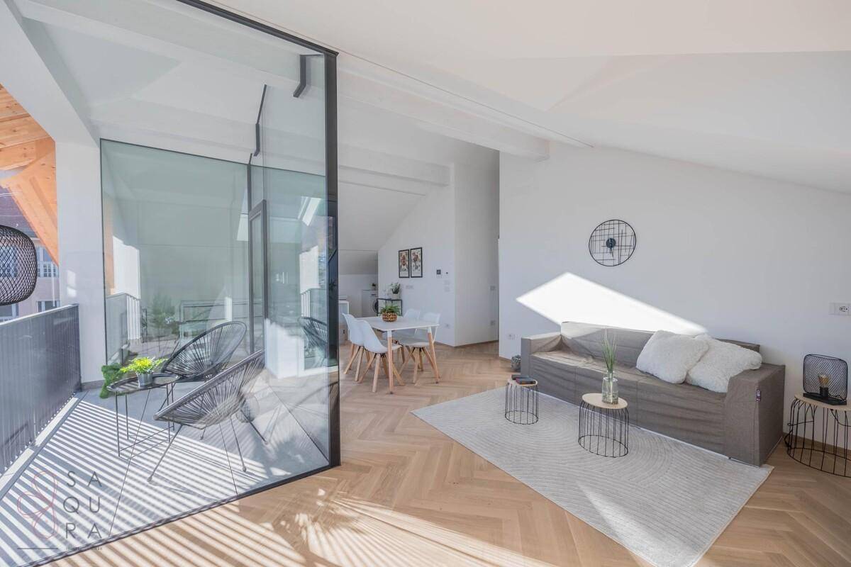 Heller Wohnbereich mit bequemer Couch, Fischgrätparkett und großem Fenster zum Balkon.