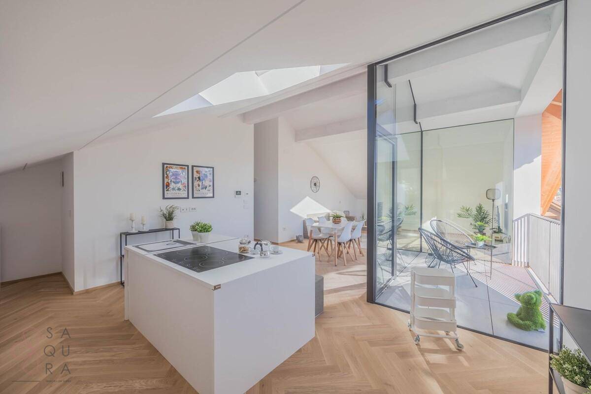Stilvolle Küche mit weißer Insel, integrierten Geräten und offenem Blick auf den Essbereich und Balkon.