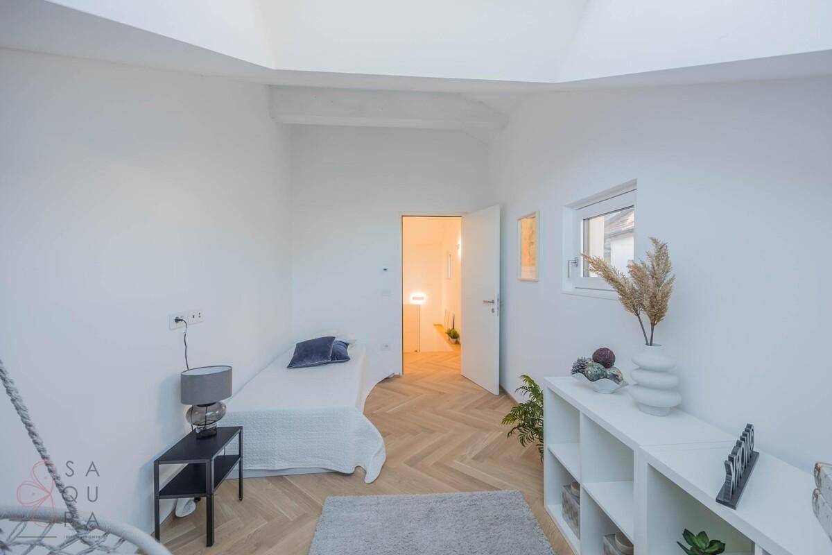 Helles Schlafzimmer mit Einzelbett, Fischgrätparkett und einem kleinen Fenster.