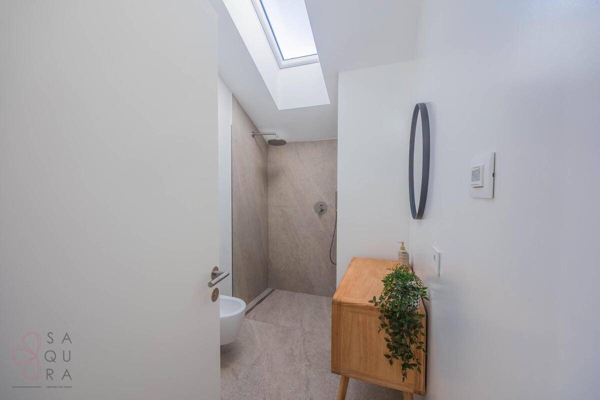 Modernes Badezimmer mit begehbarer Dusche, Bidet, Holzwaschtisch und Dachfenster für natürliches Licht.