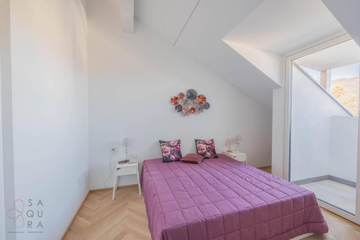 Schlafzimmer mit Doppelbett, Fischgrätparkett und einem kleinen Austritt mit Bergblick.