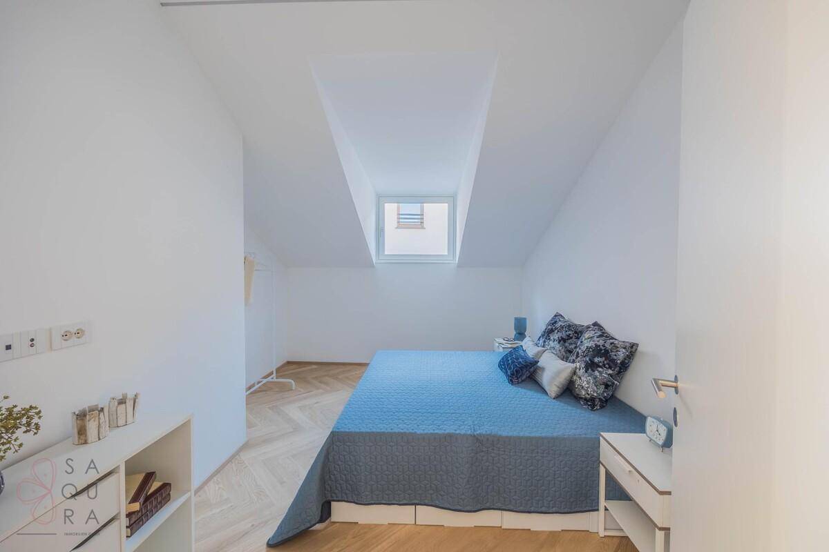 Helles Schlafzimmer mit Doppelbett, Dachfenster und Fischgrätparkett.