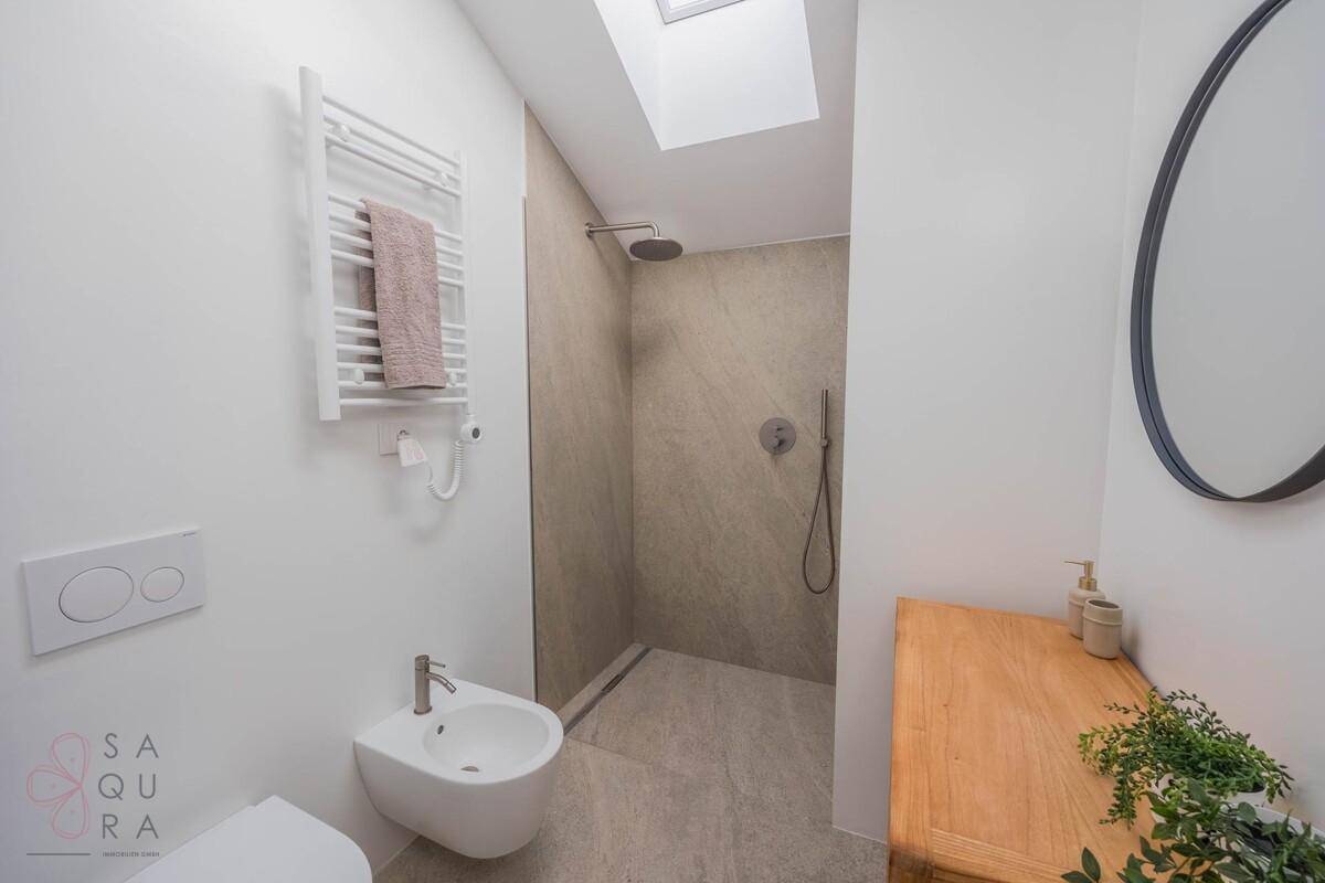 Helles Badezimmer mit moderner begehbarer Dusche, Bidet, beheiztem Handtuchhalter und Dachfenster.