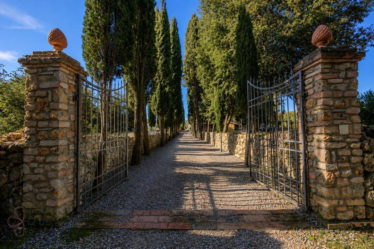 Historisches Eingangstor aus Stein und Metall führt zu einer langen Zypressenallee.