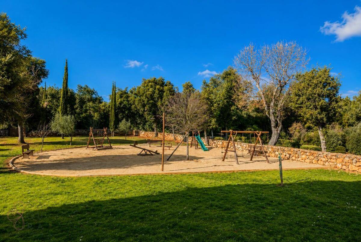 Großer Kinderspielplatz mit Schaukeln und Rutsche, umgeben von Rasen und Bäumen.