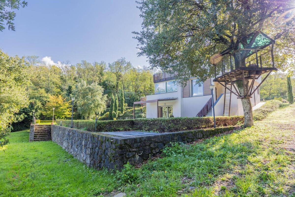 Haus mit Steinfassade, umgeben von Grünflächen und einem Baumhaus im Gartenbereich.