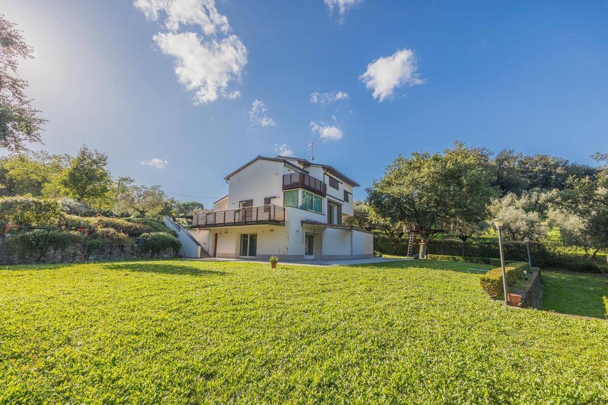 Freistehendes Haus mit weitläufigem Rasen und mediterraner Vegetation unter blauem Himmel.