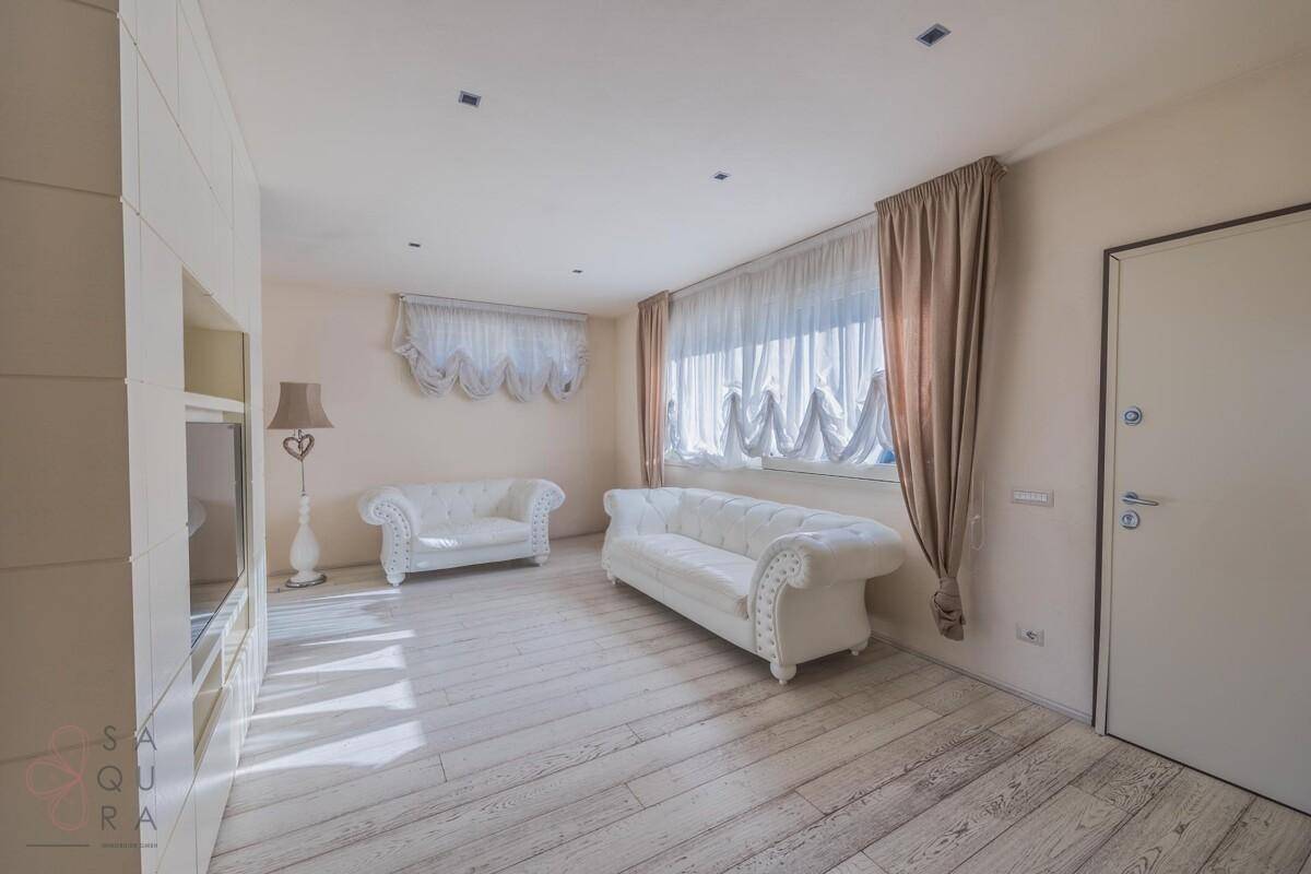 Gemütliches Wohnzimmer mit zwei weißen Sofas, hellen Vorhängen und Holzboden.