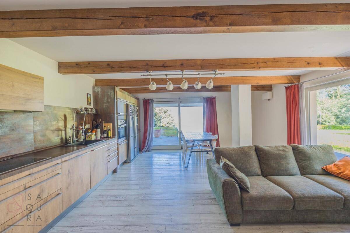 Offener Wohnbereich mit moderner Küche, Holzbalken und großen Fenstern zum Garten.