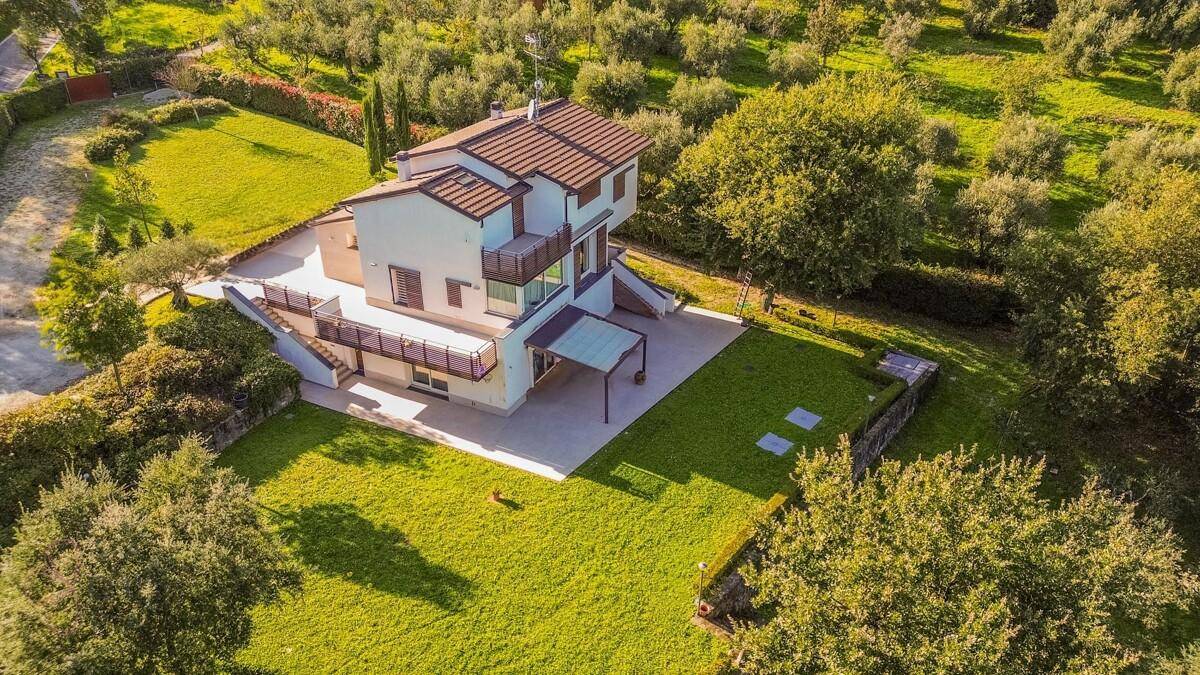 Luftaufnahme des Hauses mit gepflegtem Garten, Rasenflächen und umliegenden Bäumen.