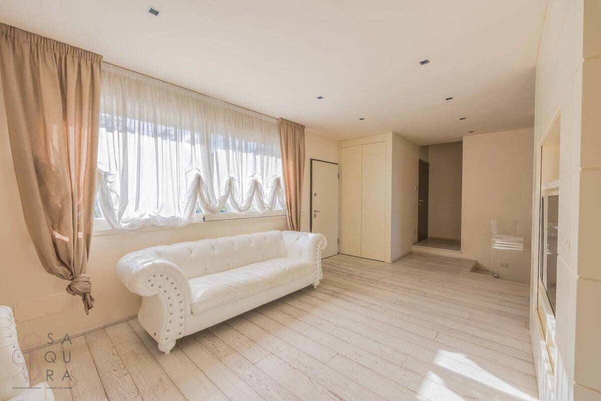 Heller Wohnbereich mit weißem Sofa, großen Fenstern und Blick auf die Landschaft.