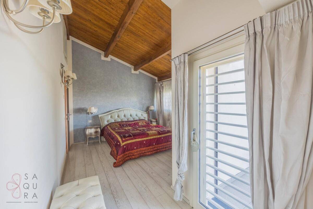 Schlafzimmer mit Holzbalkendecke, weißem Holzboden und Zugang zu einem Balkon oder einer Terrasse.