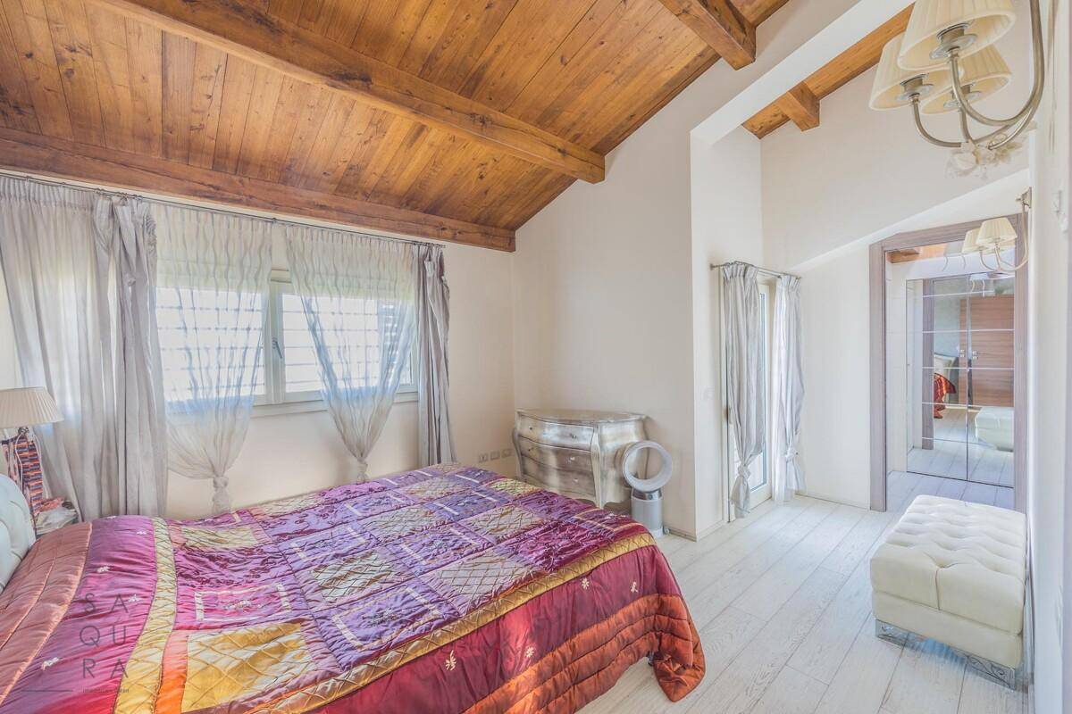 Gemütliches Schlafzimmer mit Holzbalkendecke, weißem Holzboden und einem großen Fenster mit Vorhängen.