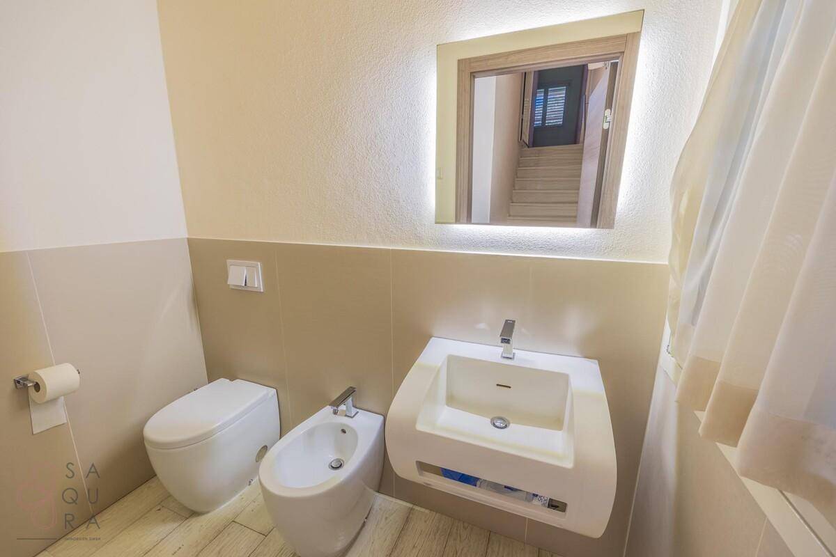 Modernes Gäste-WC mit wandmontierter Toilette, Bidet und beleuchtetem Spiegel über dem Waschbecken.