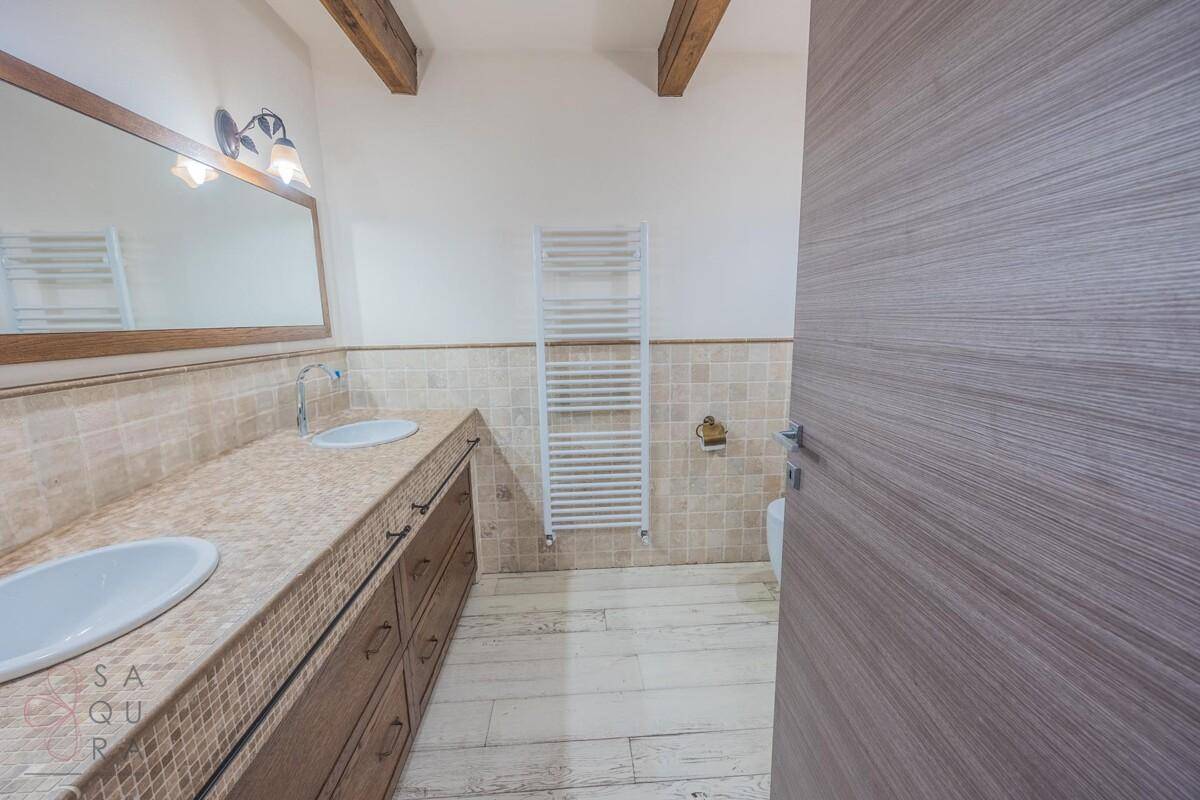 Geräumiges Badezimmer mit Doppelwaschbecken, gefliesten Wänden und sichtbaren Holzbalken an der Decke.