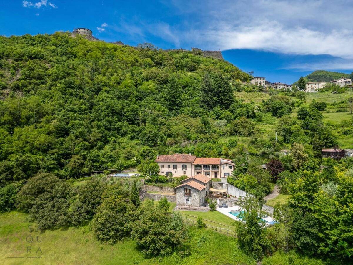 Panoramablick auf ein großes Anwesen mit mehreren Gebäuden, Pools und umgebenden grünen Hügeln.