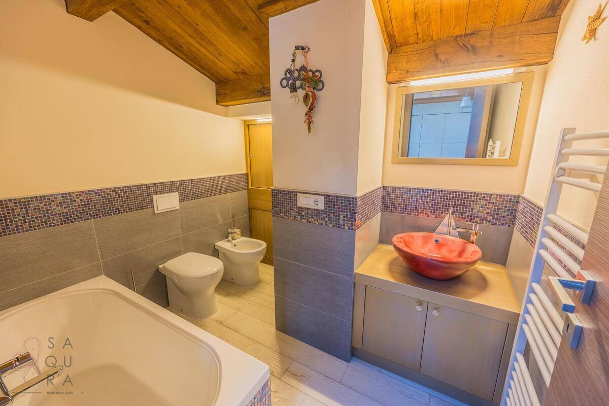 Badezimmer mit Badewanne, farbigem Waschbecken und Mosaikfliesen an den Wänden.