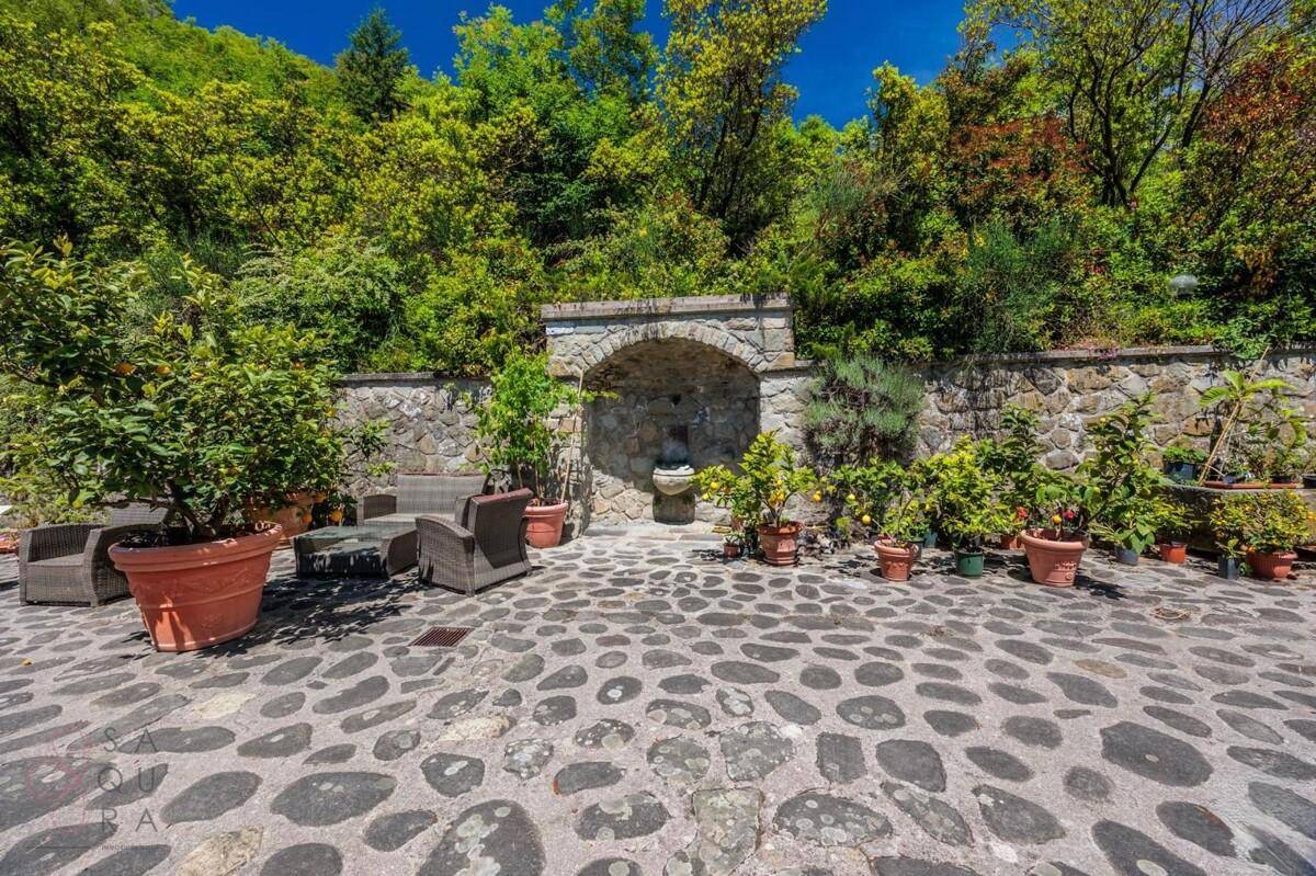 Gepflasterte Terrasse mit Sitzgelegenheiten, Topfpflanzen und einem Steinbrunnen in einer Nische.