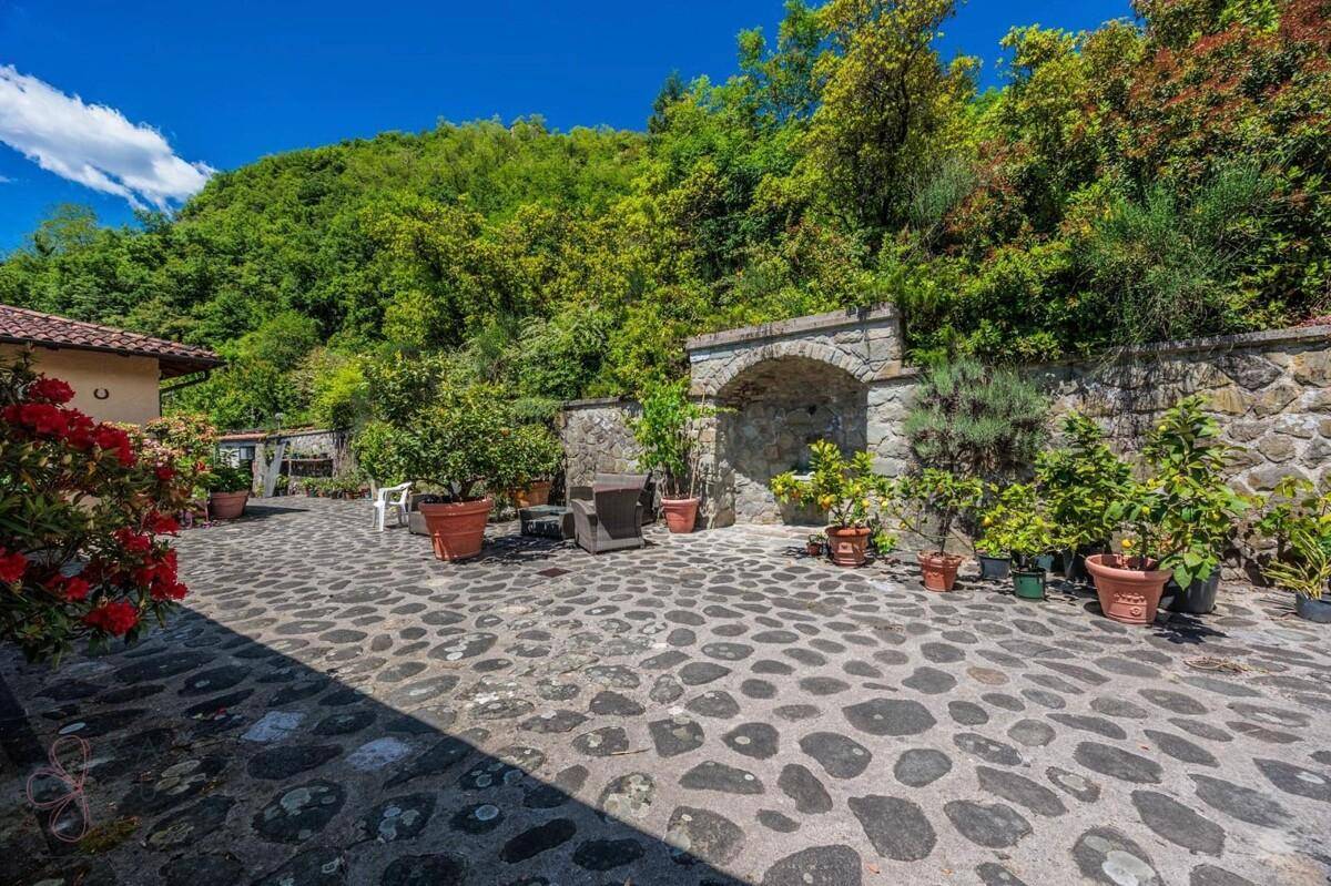 Weitläufiger gepflasterter Patio mit Steinmauer, Brunnen und verschiedenen Topfpflanzen.